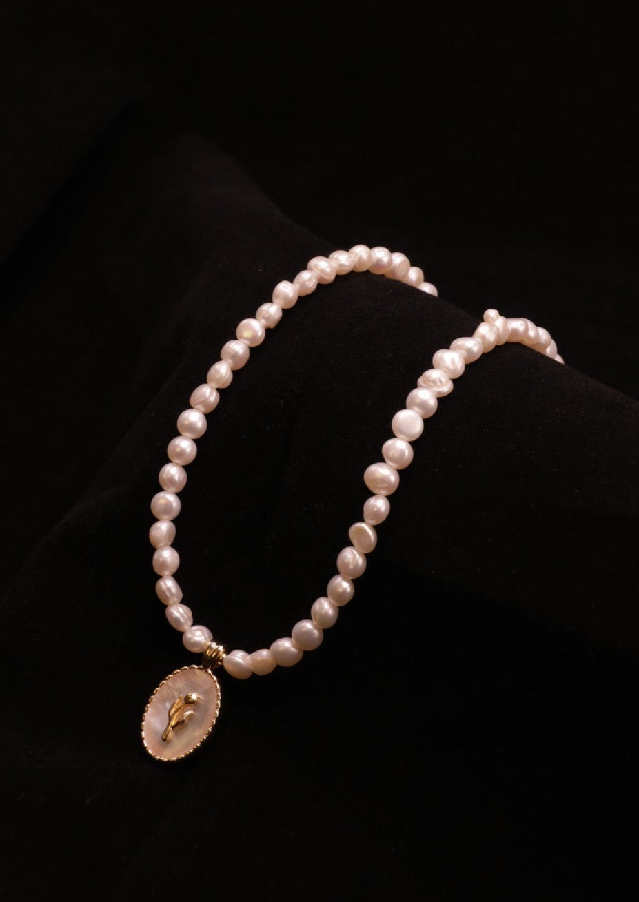 A delicate pearl necklace featuring small white pearls strung together, with a gold-plated pendant at the centre. The pendant is oval-shaped, with a mother of pearl base and a gold tulip design in the middle. The necklace is adjustable, with a length ranging from 38 to 43 cm (14.9 to 16.9 inches).