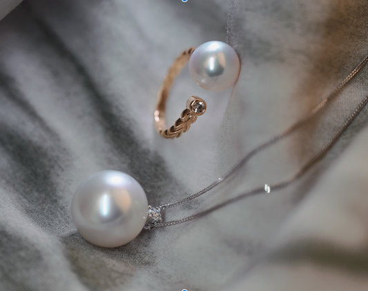 Image of a 10.2mm Akoya pearl open ring featuring a diamond at one end, paired with a premium 14.8mm South Sea white pearl necklace, set against a soft, neutral fabric background.